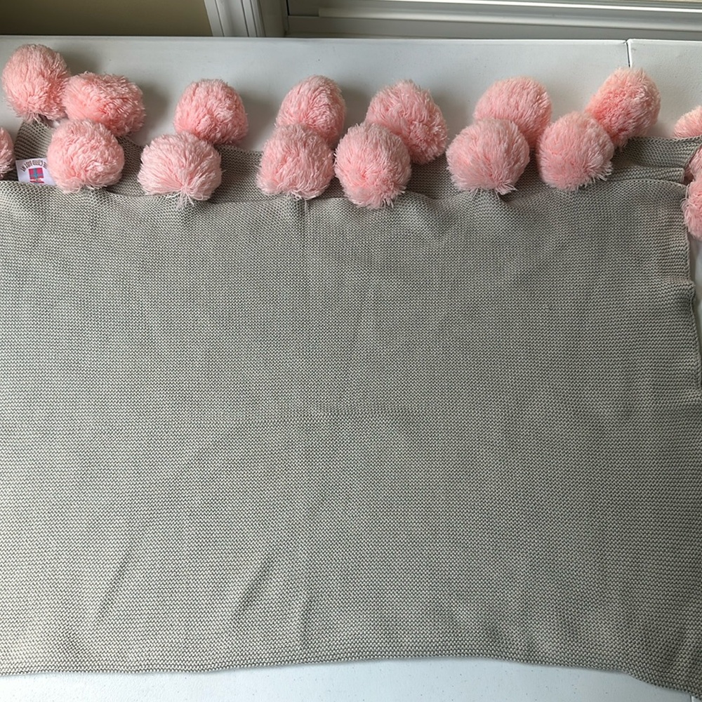 Gray knitted baby blanket with pink pom-poms